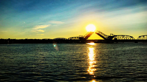 Silhouette bridge over river against sky during sunset