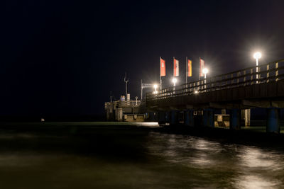 Illuminated bridge over river against sky at night