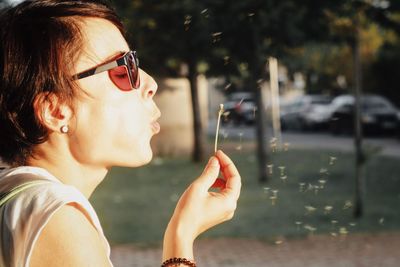 Side view of woman blowing dandelion outdoors