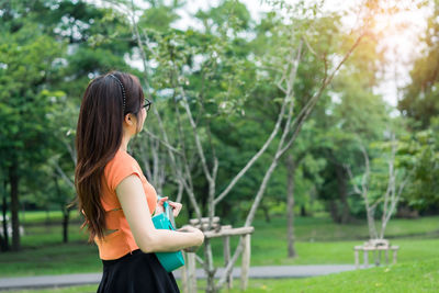 Side view of young woman standing against trees