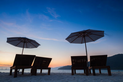 Chairs on beach against sky during sunset