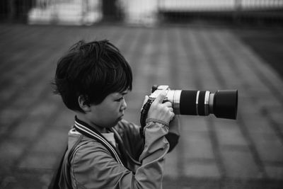 Side view of boy photographing while standing outdoors