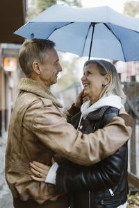 Side view of romantic mature couple standing under umbrella at street