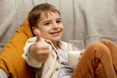 Little adorable boy sitting on the couch at home and drinking milk. fresh milk in glass