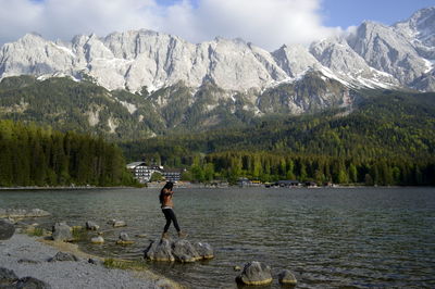 Man standing on rock by lake against mountains
