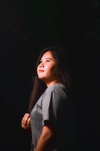 Woman looking away while standing against black background