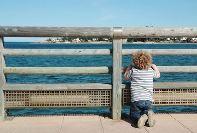 Rear view of boy looking at sea through wooden railing