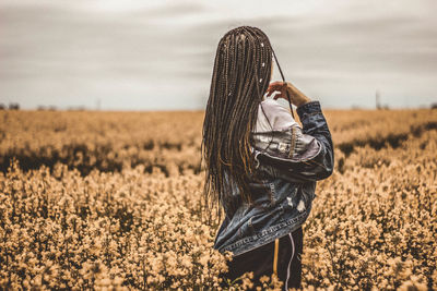 Rear view of woman with braided hair standing amidst flowers on land