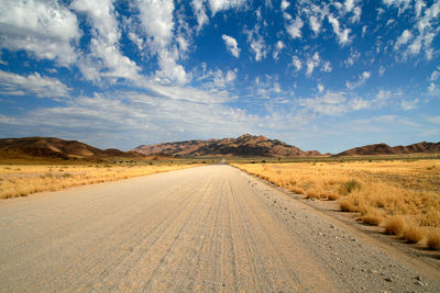 Dirt road amidst land against sky