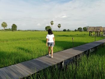 Woman standing on walkway amidst field against sky