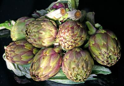 Beautiful fresh purple and green artichokes with green leaves on black background, close up