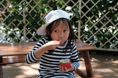 Cute girl eating ice cream against fence