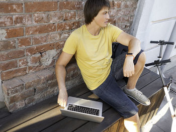 Man sits with laptop and kick scooter in cafe. freelancer. student learns remotely from outdoors. 