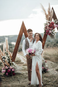 Young couple holding pink flower against plants