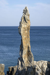 Candle rock by sea against sky