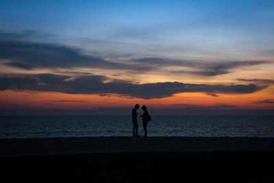 Silhouette couple standing on beach against sky during sunset