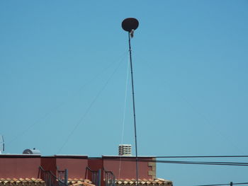 Low angle view of satellite dish and cable over buildings against blue sky