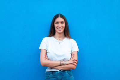 Portrait of smiling young woman standing against blue wall