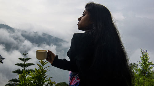 Young woman holding coffee cup against mountains
