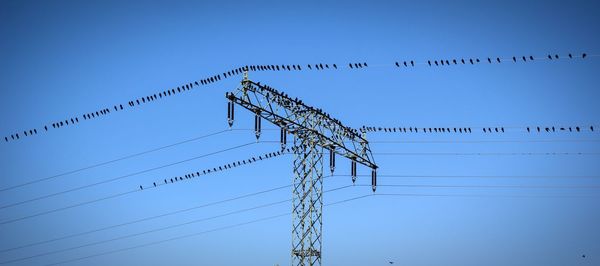 Low angle view of electricity pylon against clear blue sky