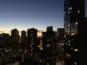 Illuminated buildings in city against clear sky