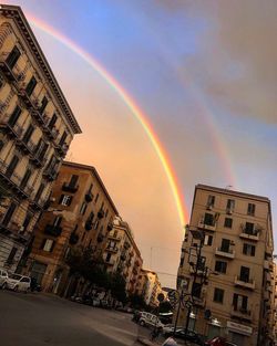 Rainbow over buildings in city against sky at sunset