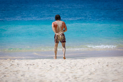 A man runs to swim in the blue sea. the back of the body is covered with sand.