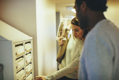 Young woman with male friend looking at mailbox in college dorm corridor