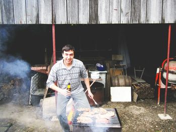Portrait of smiling man cooking barbecue grill while standing against yard