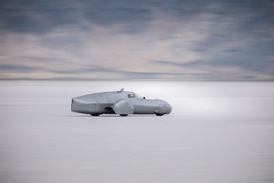 Vehicle moving on snow covered field against cloudy sky