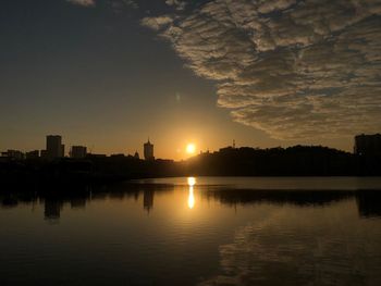 Scenic view of lake by silhouette buildings against sky during sunset