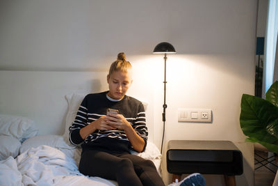 Woman using her phone when sitting on bed