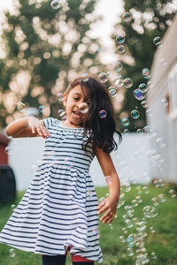 Diverse mixed race pre school girl outdoors during summer having fun in backyard with bubbles 