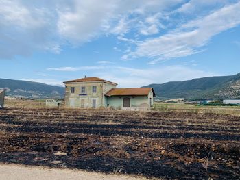 House on field by buildings against sky