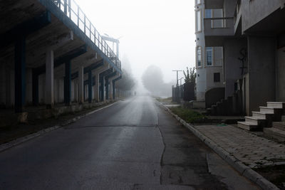 Empty road amidst buildings against sky in city