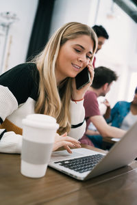 Young woman using mobile phone while sitting on table