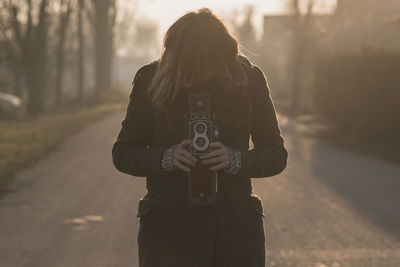 Young woman photographing through camera on road