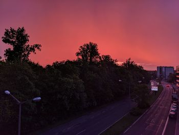 Road by trees against sky at sunset