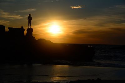 Silhouette man standing by sea against sky during sunset