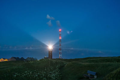 Illuminated lighthouse and buildings against sky at night