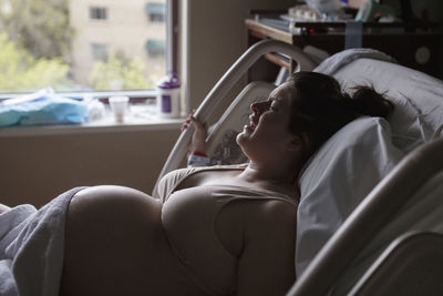 Side view of painful pregnant woman lying on hospital bed