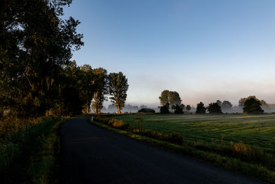 Road by trees on field against sky