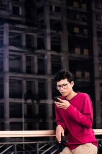 Young woman looking down while standing against building