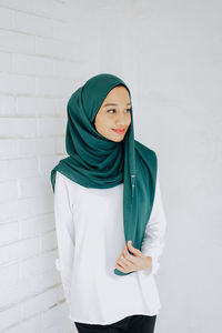 Young woman in headscarf looking away against wall