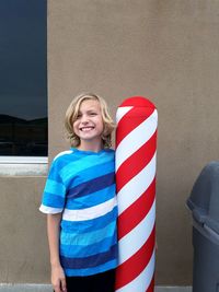 Portrait of cheerful boy standing by striped bollard on footpath