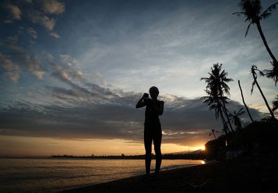 Side view of woman standing on beach against sky during sunset