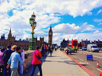 People walking in city against cloudy sky