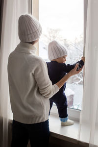 Mother and son in hats standing at the window in winter