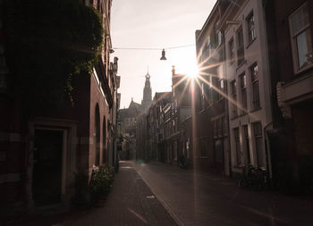 Narrow alley amidst buildings in city against bright sun