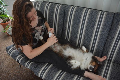 High angle view of mid adult woman grooming dog on sofa at home